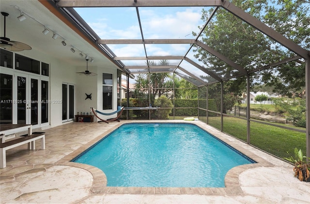 view of swimming pool with a lawn, french doors, ceiling fan, glass enclosure, and a patio area