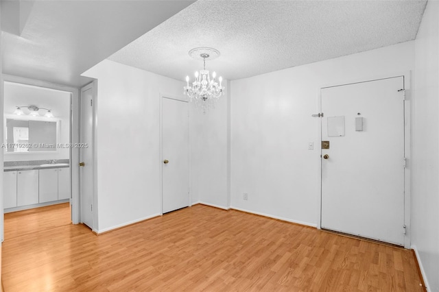 spare room with light wood-type flooring, a textured ceiling, and an inviting chandelier