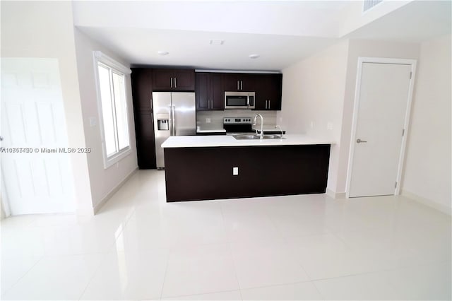 kitchen featuring sink, dark brown cabinetry, light tile patterned flooring, kitchen peninsula, and stainless steel appliances