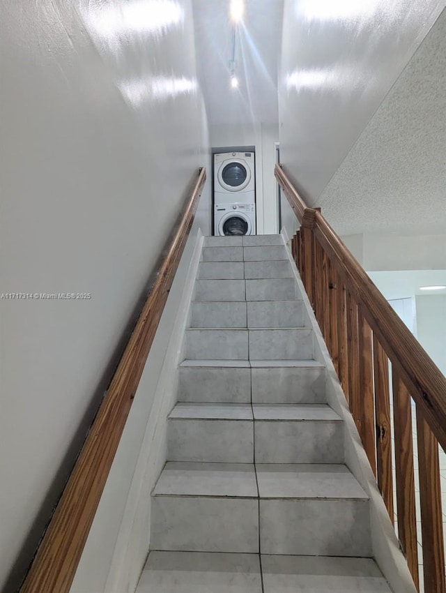 staircase featuring a textured ceiling and stacked washer and clothes dryer