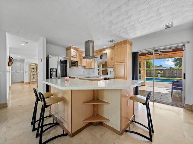 kitchen featuring light brown cabinetry, a breakfast bar area, island range hood, stainless steel fridge, and a kitchen island