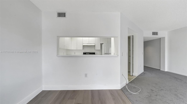 interior space featuring white fridge, hardwood / wood-style floors, white cabinets, and a textured ceiling