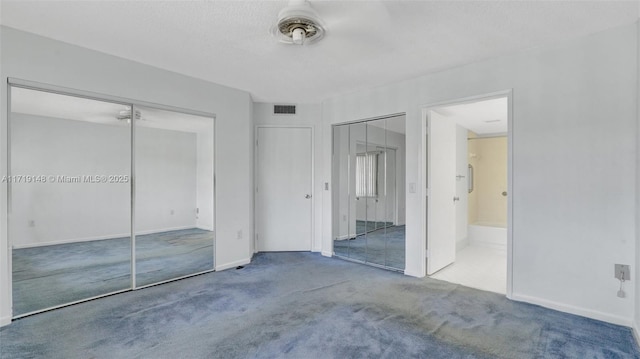 unfurnished bedroom featuring carpet flooring, two closets, and a textured ceiling