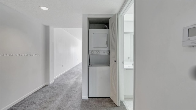 hall featuring stacked washing maching and dryer, carpet, and a textured ceiling