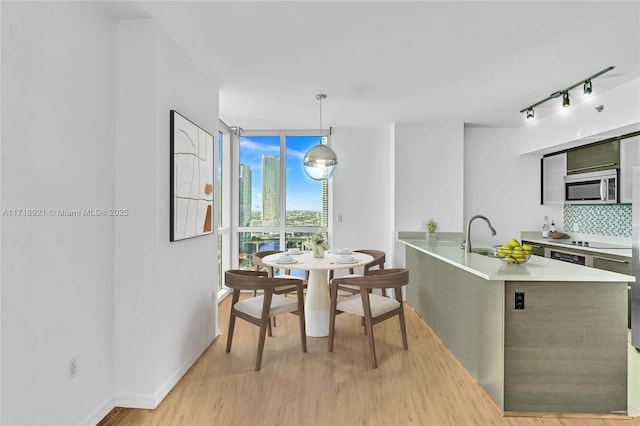 kitchen with decorative backsplash, light wood-type flooring, rail lighting, sink, and hanging light fixtures