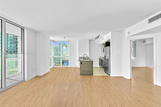 unfurnished living room with light hardwood / wood-style floors, a wall of windows, and sink