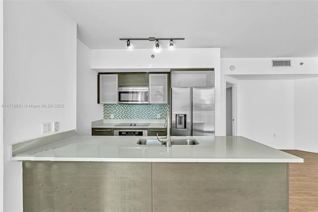 kitchen featuring kitchen peninsula, appliances with stainless steel finishes, light wood-type flooring, decorative backsplash, and sink