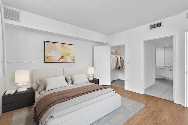 bedroom featuring a walk in closet, ensuite bathroom, a closet, and light wood-type flooring