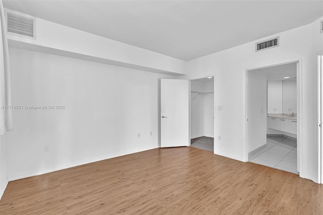 unfurnished bedroom featuring connected bathroom, a spacious closet, a closet, and light wood-type flooring