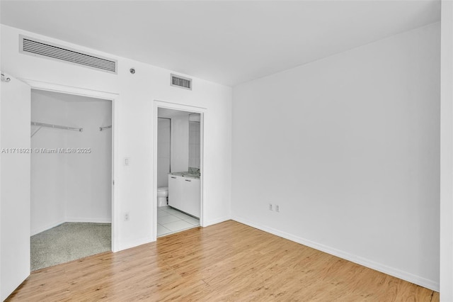 unfurnished bedroom featuring light wood-type flooring, a closet, and connected bathroom