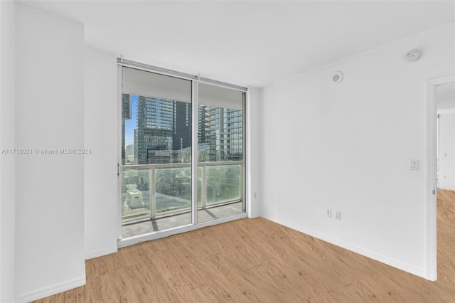 unfurnished room with a wall of windows and light hardwood / wood-style flooring