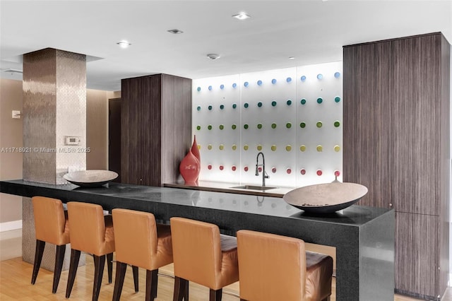 bar featuring dark brown cabinets, light hardwood / wood-style flooring, and sink