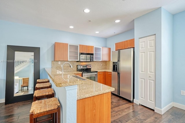 kitchen featuring stainless steel appliances, dark hardwood / wood-style floors, backsplash, kitchen peninsula, and a breakfast bar area