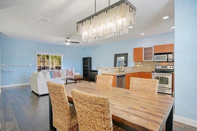 dining area featuring ceiling fan with notable chandelier, sink, and dark wood-type flooring