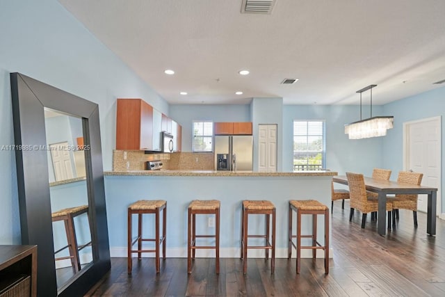 kitchen featuring stainless steel fridge with ice dispenser, kitchen peninsula, hanging light fixtures, and a breakfast bar area