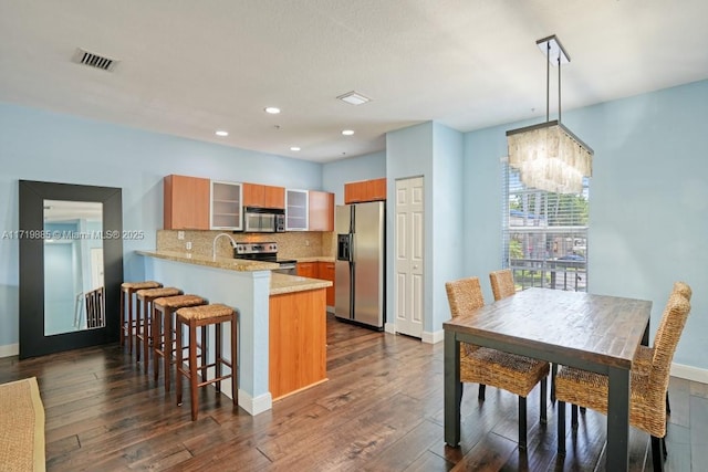 kitchen featuring appliances with stainless steel finishes, tasteful backsplash, decorative light fixtures, kitchen peninsula, and a breakfast bar area