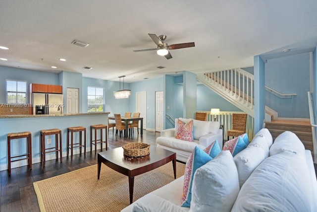 living room with ceiling fan with notable chandelier and dark hardwood / wood-style flooring