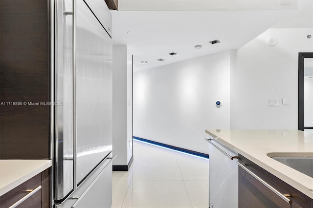 kitchen featuring dark brown cabinetry, light tile patterned flooring, and appliances with stainless steel finishes