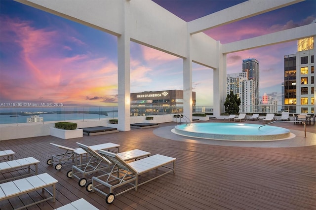 pool at dusk with a water view and a hot tub