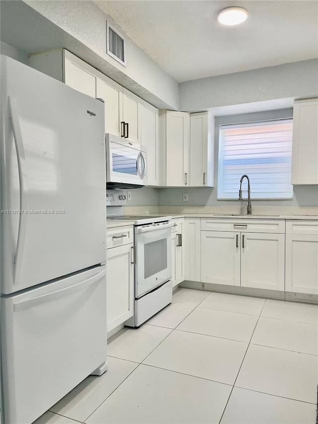 kitchen with white cabinets, white appliances, sink, and light tile patterned floors