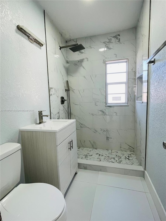 bathroom with a tile shower, tile patterned flooring, vanity, and toilet