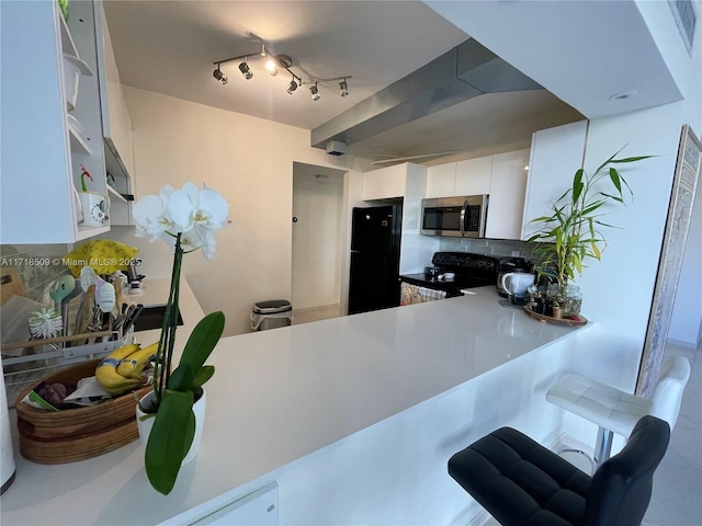 kitchen with backsplash, kitchen peninsula, white cabinetry, and black appliances