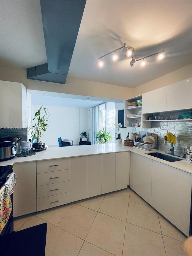 kitchen with decorative backsplash, stove, sink, white cabinets, and light tile patterned flooring