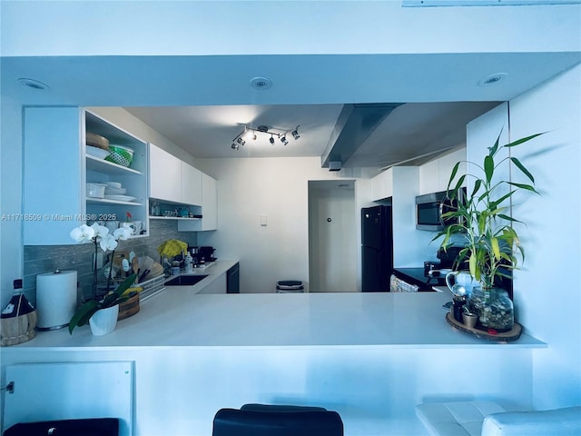 kitchen featuring black refrigerator, white cabinetry, sink, and tasteful backsplash