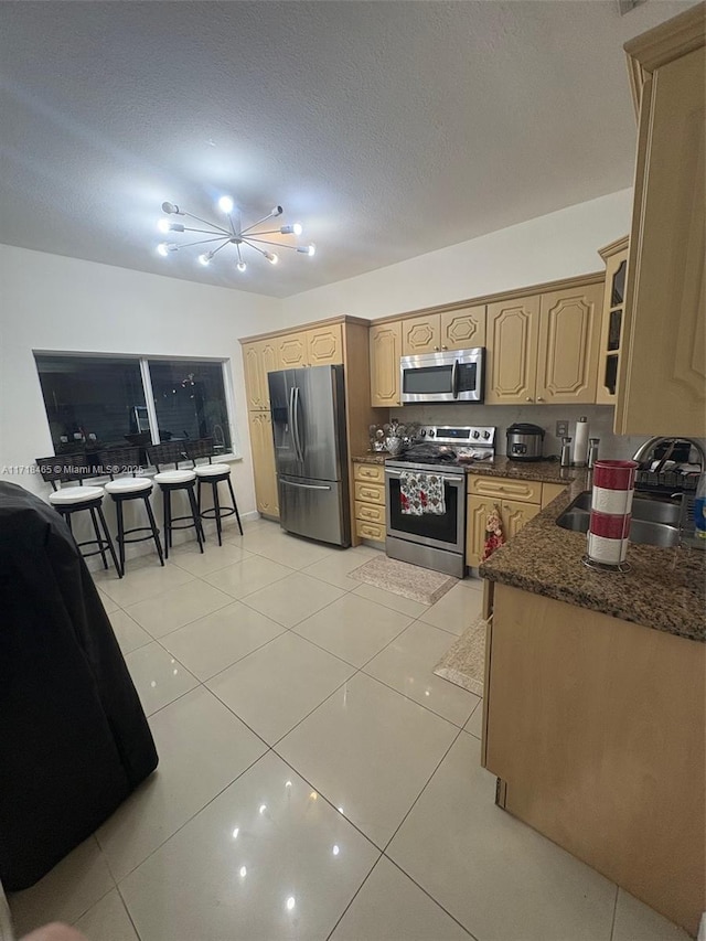 kitchen with dark stone countertops, sink, light tile patterned floors, and appliances with stainless steel finishes