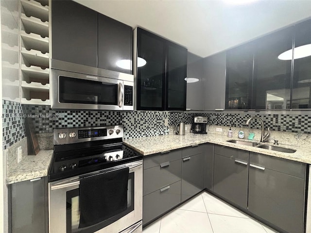 kitchen with backsplash, sink, light stone countertops, light tile patterned flooring, and stainless steel appliances