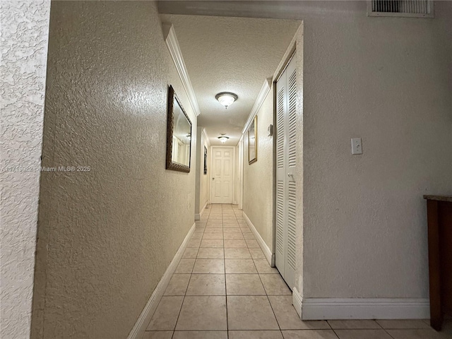 hallway featuring light tile patterned floors, a textured ceiling, and crown molding