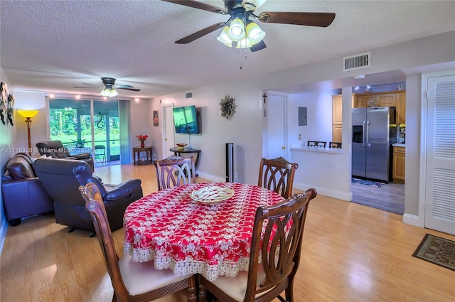 dining area featuring electric panel, ceiling fan, light hardwood / wood-style floors, and a textured ceiling