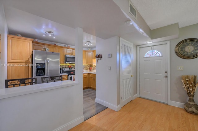 kitchen with decorative backsplash, light brown cabinets, stainless steel appliances, and light hardwood / wood-style flooring