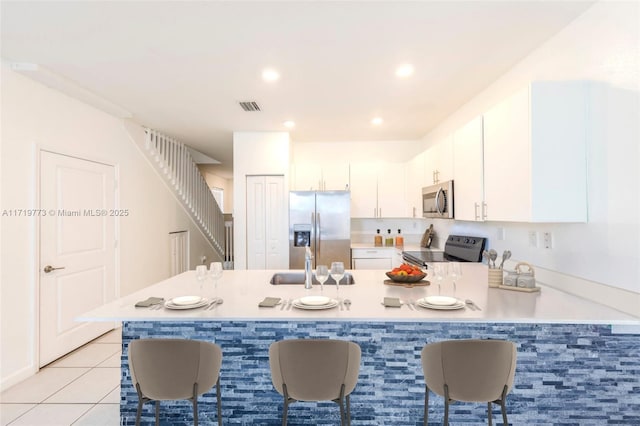 kitchen featuring white cabinetry, light tile patterned flooring, a kitchen bar, kitchen peninsula, and stainless steel appliances