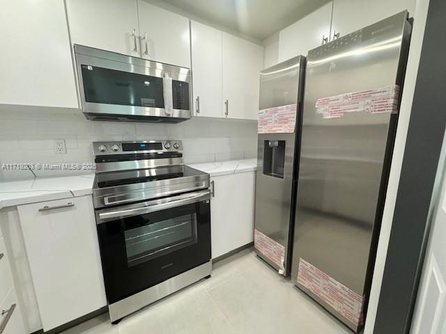 kitchen with white cabinets, light tile patterned flooring, light stone counters, and appliances with stainless steel finishes