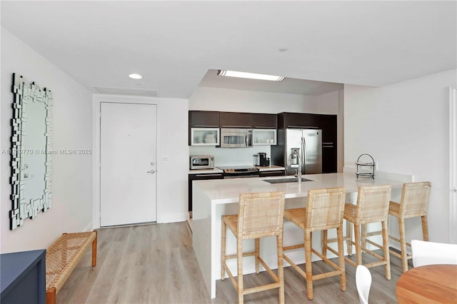 kitchen with a breakfast bar, light hardwood / wood-style floors, sink, and appliances with stainless steel finishes