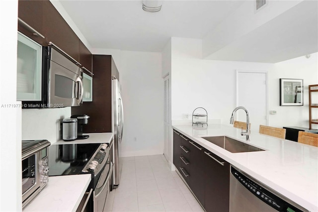 kitchen with dark brown cabinetry, sink, light tile patterned flooring, and appliances with stainless steel finishes