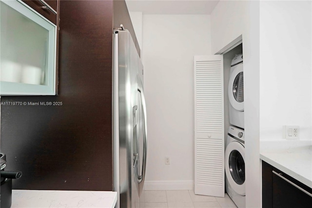 laundry area with stacked washer / drying machine and light tile patterned flooring