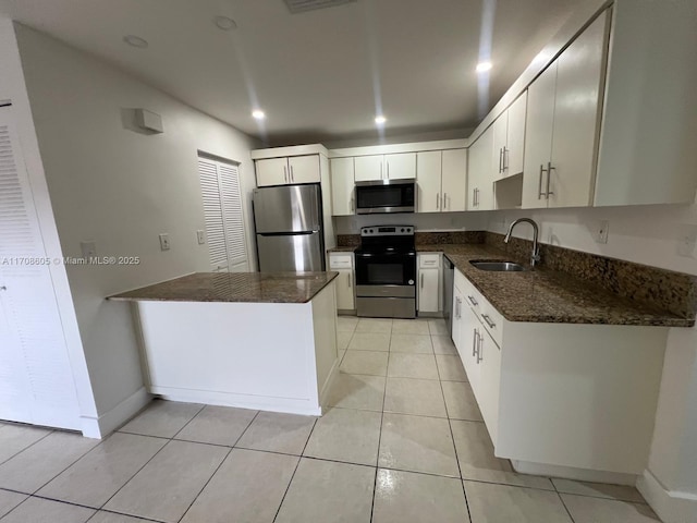 kitchen with dark stone counters, stainless steel appliances, sink, light tile patterned floors, and white cabinetry