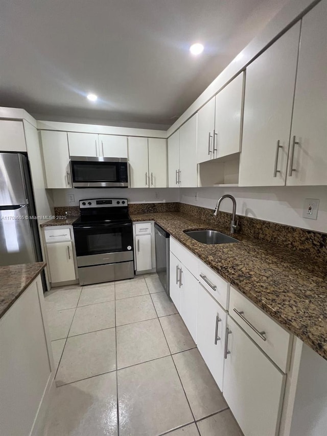 kitchen with white cabinetry, sink, dark stone countertops, light tile patterned floors, and appliances with stainless steel finishes