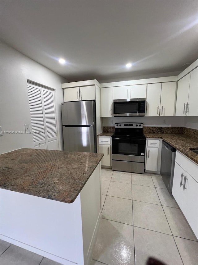 kitchen featuring white cabinets, dark stone counters, light tile patterned floors, and appliances with stainless steel finishes