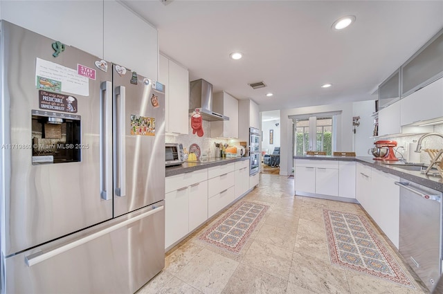 kitchen featuring sink, wall chimney range hood, decorative backsplash, white cabinets, and appliances with stainless steel finishes