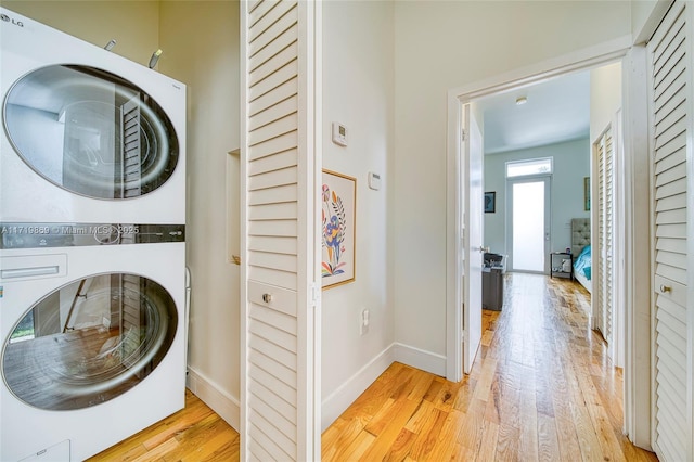 clothes washing area with stacked washing maching and dryer and light hardwood / wood-style flooring