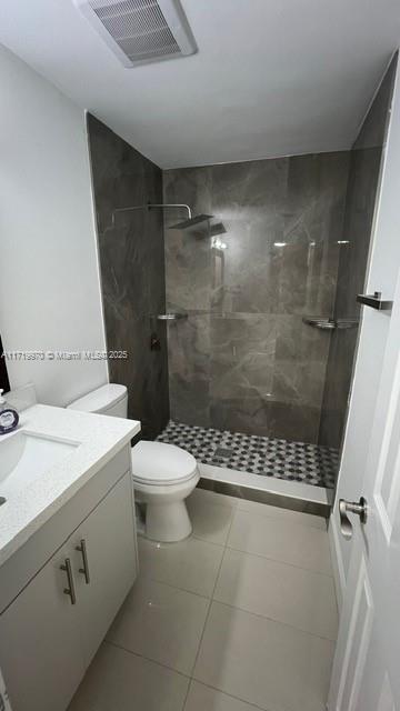 bathroom featuring tiled shower, vanity, toilet, and tile patterned flooring