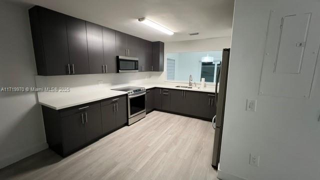 kitchen with appliances with stainless steel finishes, sink, and light wood-type flooring