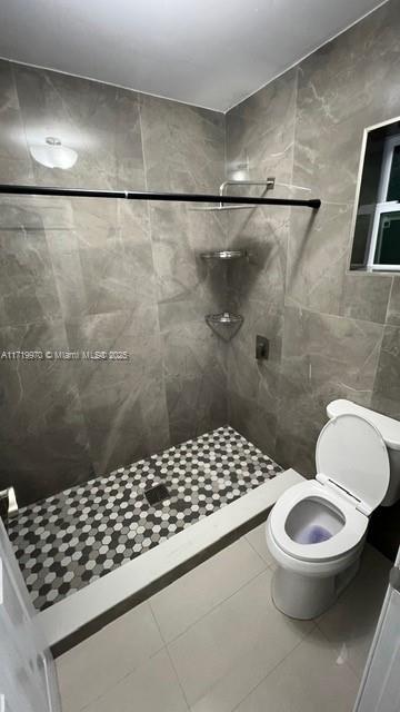 bathroom with tiled shower, toilet, and tile patterned flooring