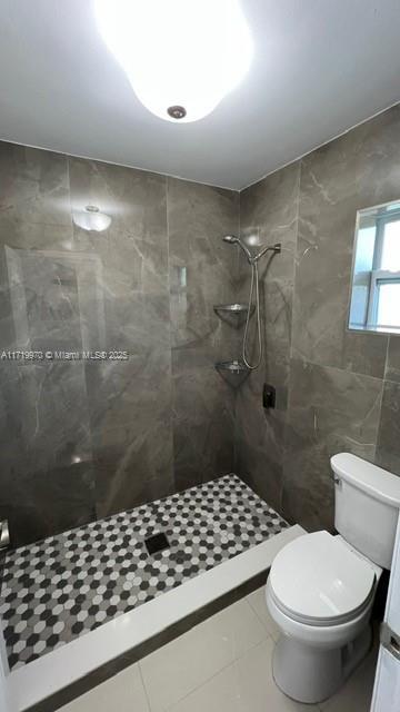 bathroom with tile patterned flooring, toilet, and tiled shower