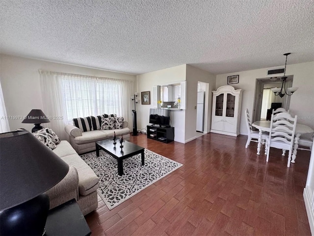 living room with dark hardwood / wood-style flooring, a textured ceiling, and an inviting chandelier