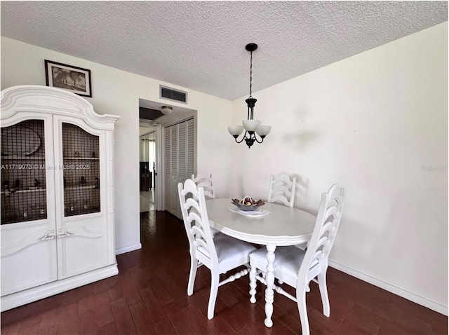 dining area with dark hardwood / wood-style floors, a textured ceiling, and a notable chandelier