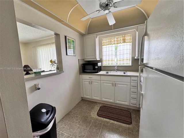 kitchen featuring a wealth of natural light, white cabinetry, sink, and white fridge